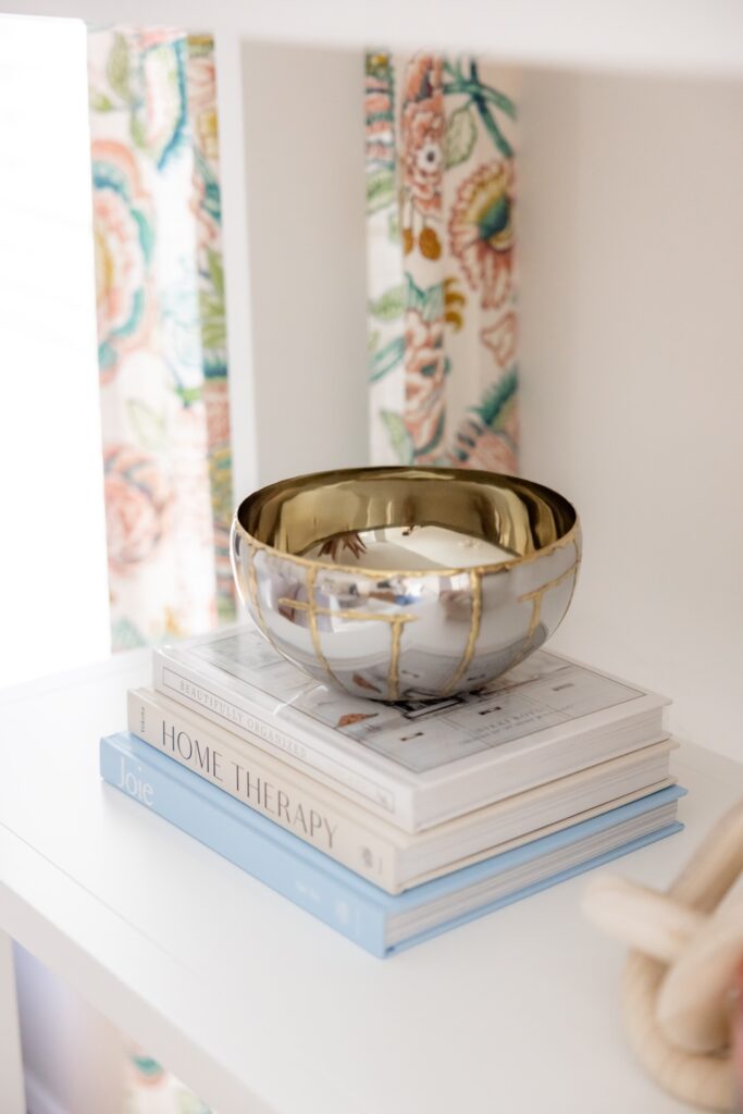A silver bowl sitting on a stack of decorative books on top of a bookcase.
