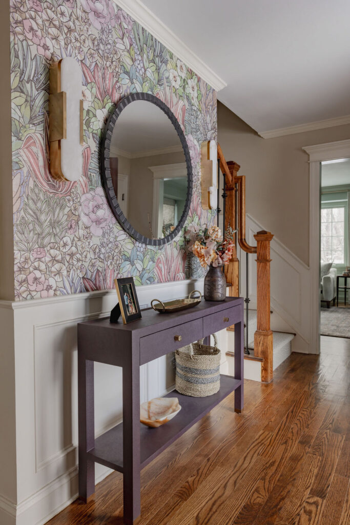 A gorgeous aubergine console table in an entryway with floral wallpaper and accessories.