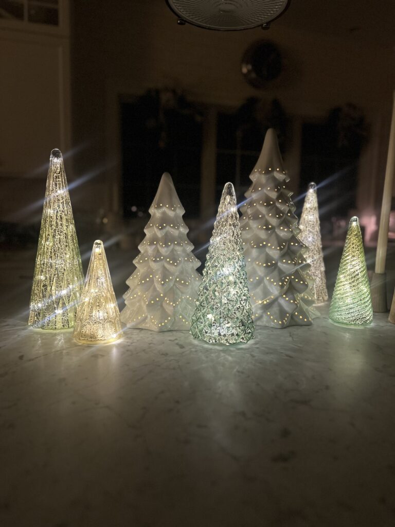 Collection of illuminated glass and ceramic Christmas trees displayed on a marble countertop, creating a soft, modern holiday glow.
